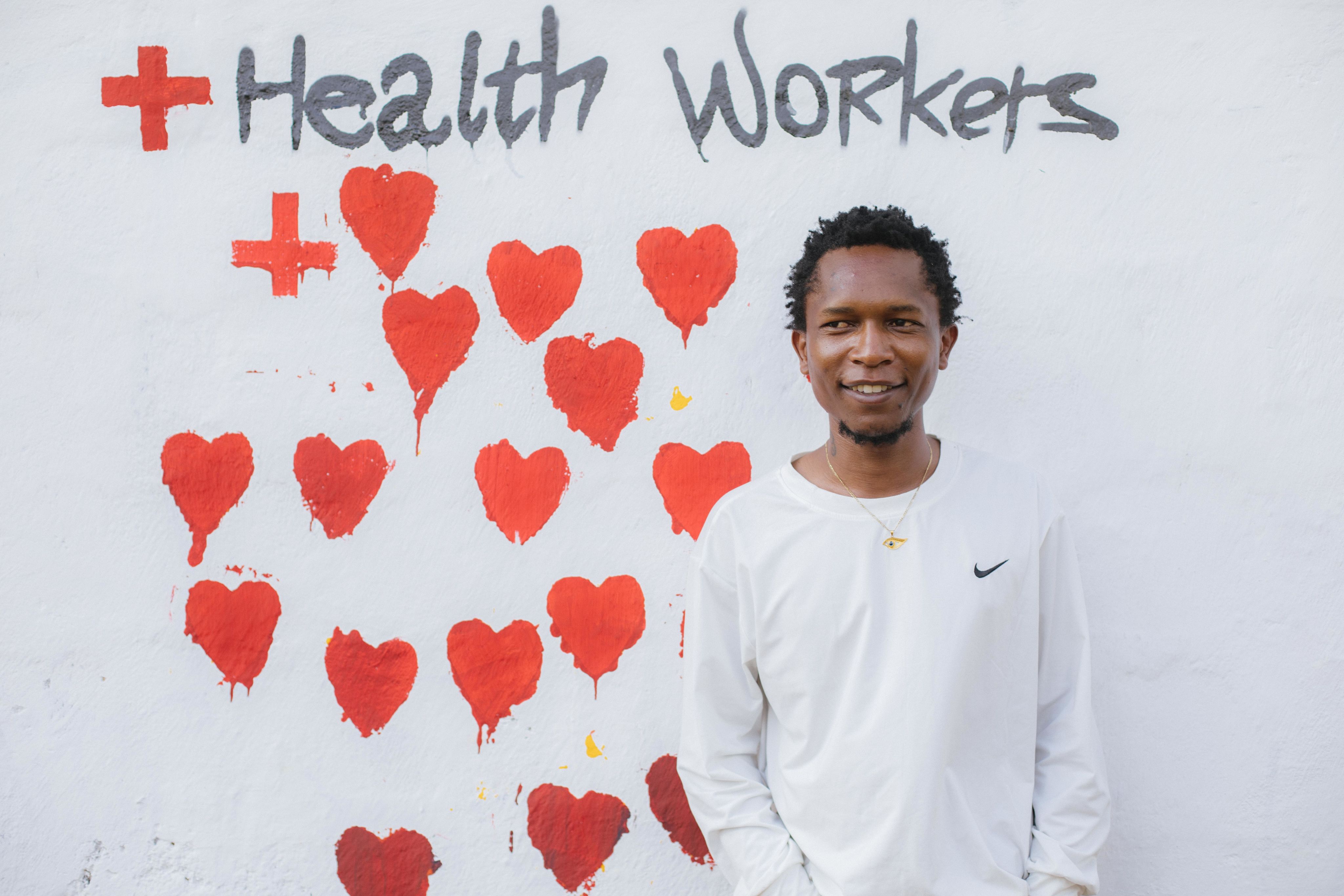 Stephen standing next to a big number of red hearts that show appreciation for health workers.